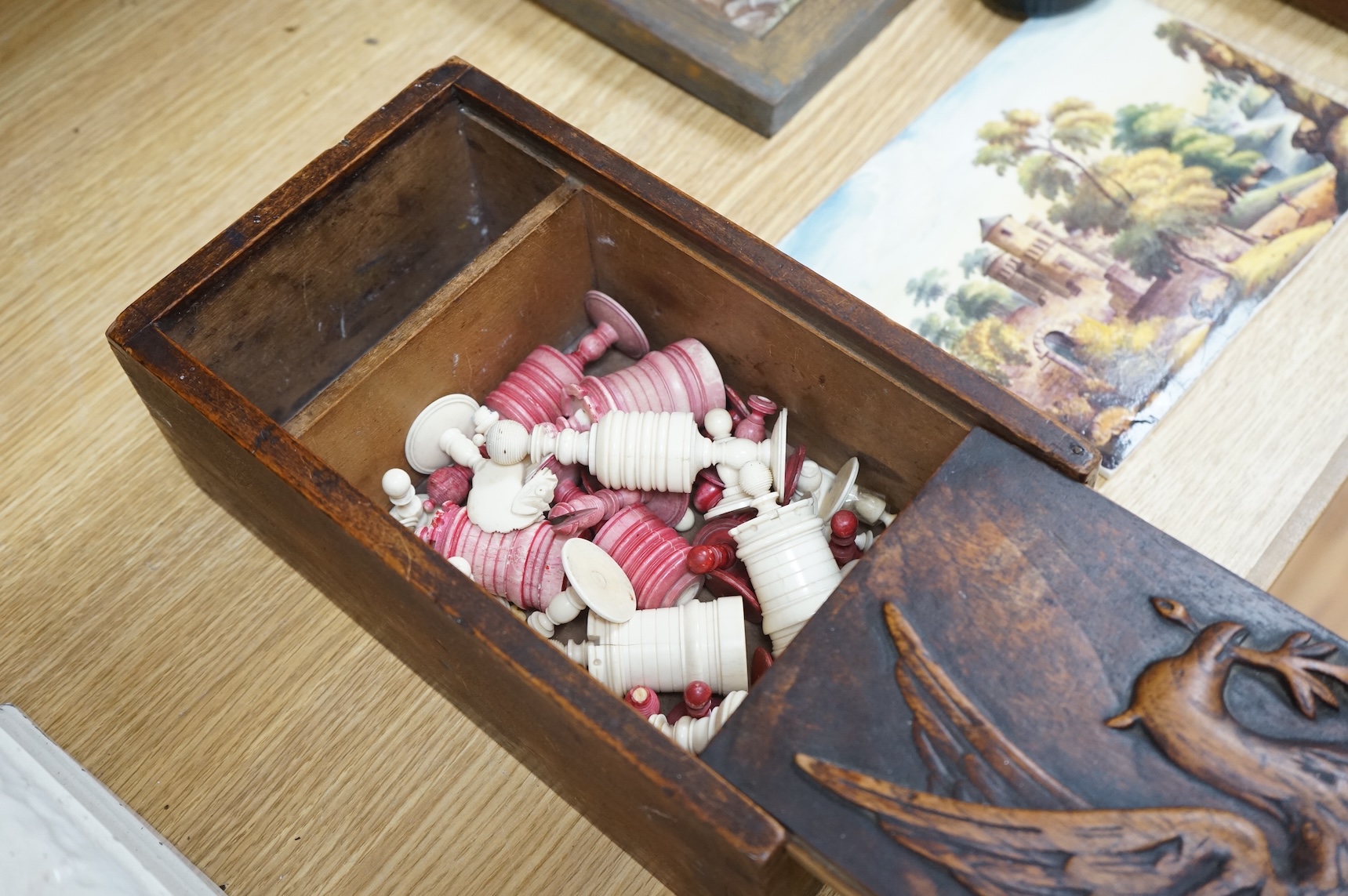 A 19th century games box with sliding cover carved with an eagle. The box containing a part bone stained chess set, box 28cm deep